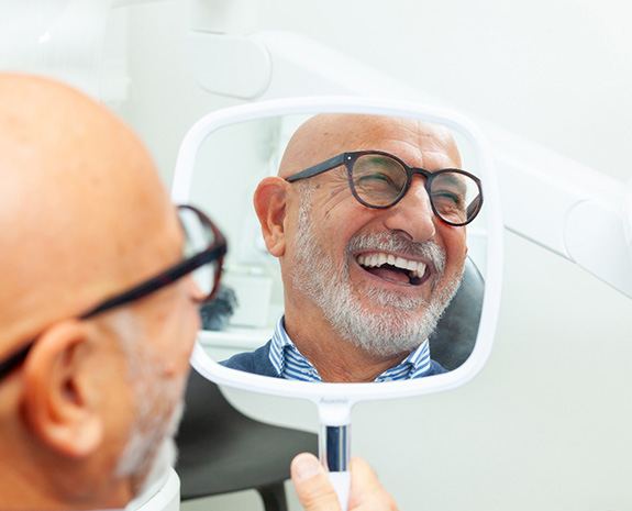 A man smiling in the mirror at his dental implants