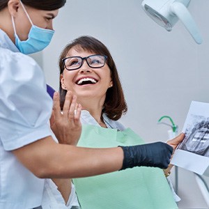 Woman smiling with dentist while reviewing X-ray