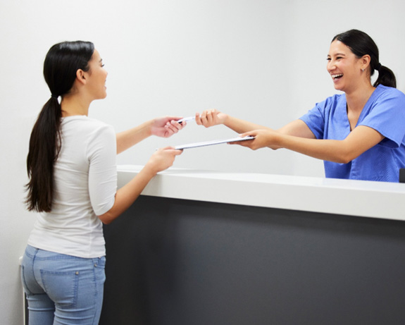 Smiling dental assistant handing patient form