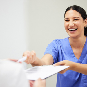 Smiling dental assistant handing patient forms
