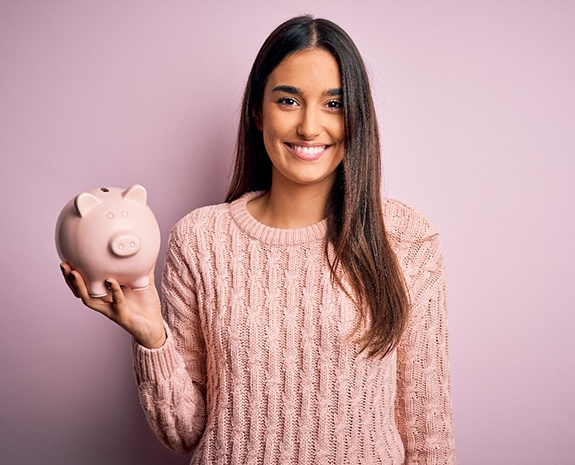 Smiling woman in pink sweater holding pink piggy bank with pink background